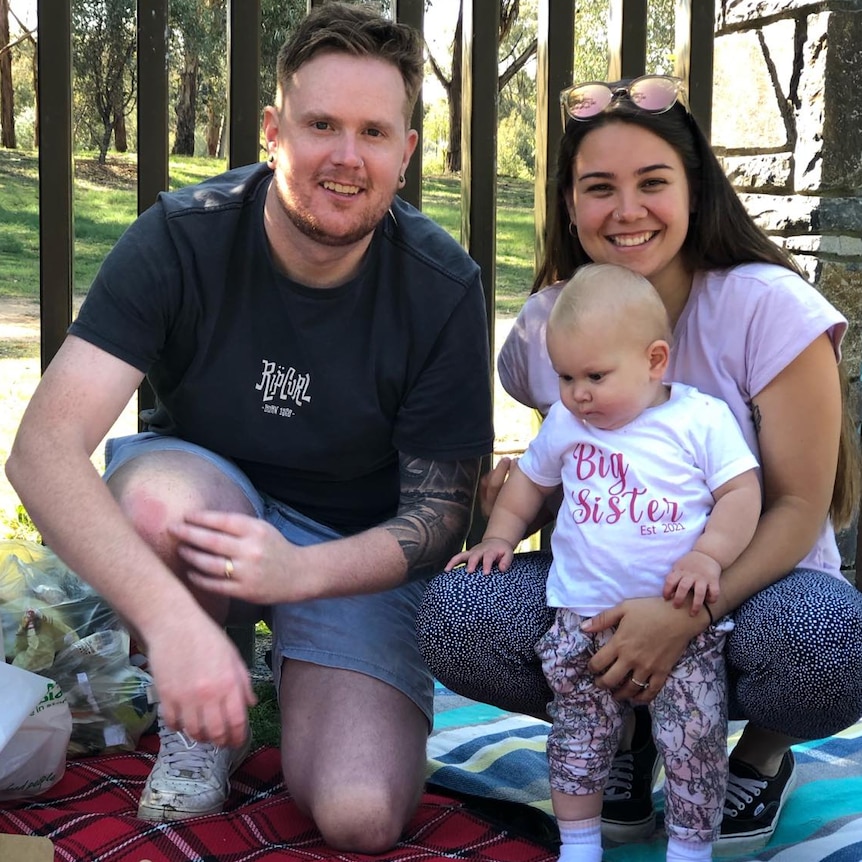 A woman with brown hair smiles with a man and a baby