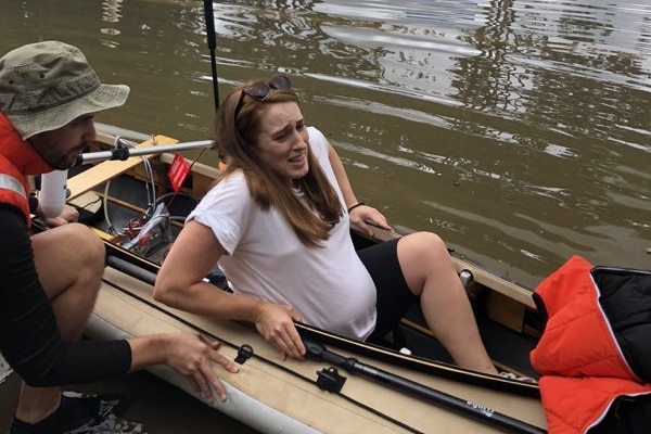 A man assisting a pregnant woman sitting in a kayak.