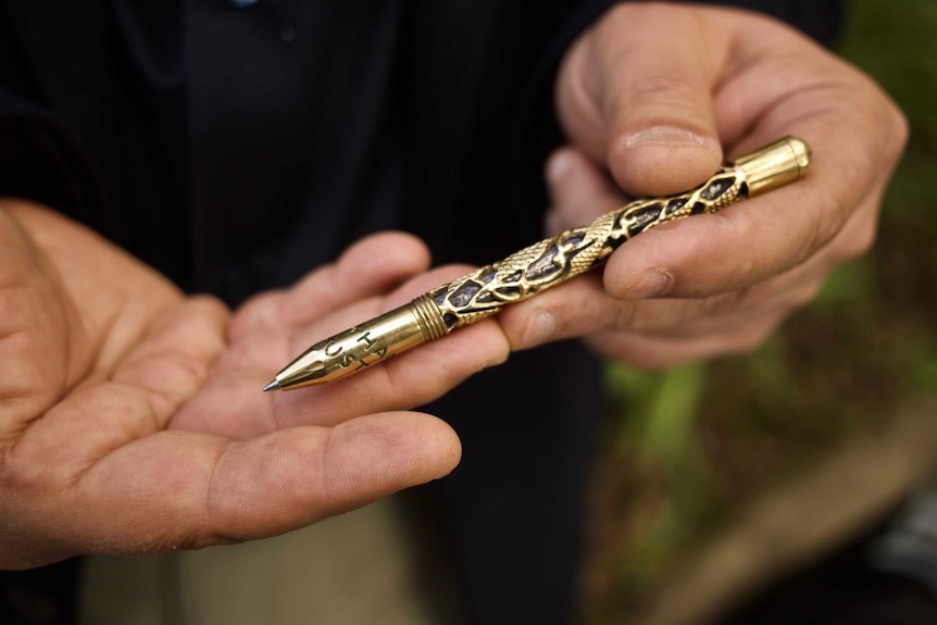 Close up of Sameer Dakhil's hands holding a golden carved pen.