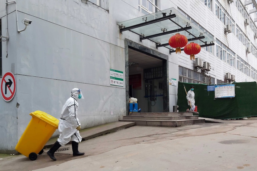 A staff member wearing a hazardous materials suit hauls a bin at a hospital.