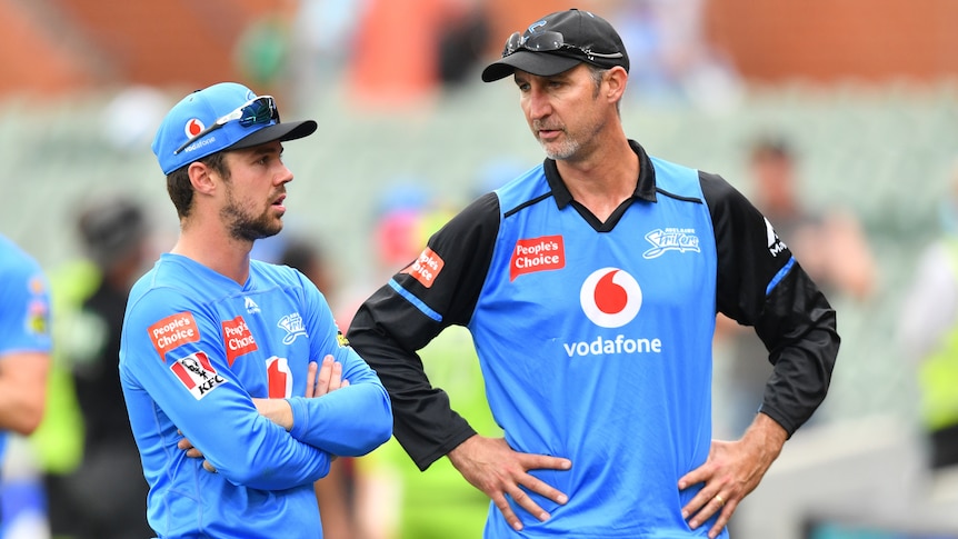 Cricket coach standing with his hands on his hips while talking to one of his player after a match