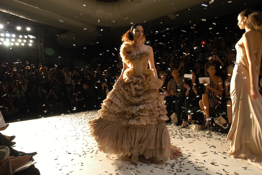 Photo of a model in a frilly dress walking down the catwalk with confetti falling over her.