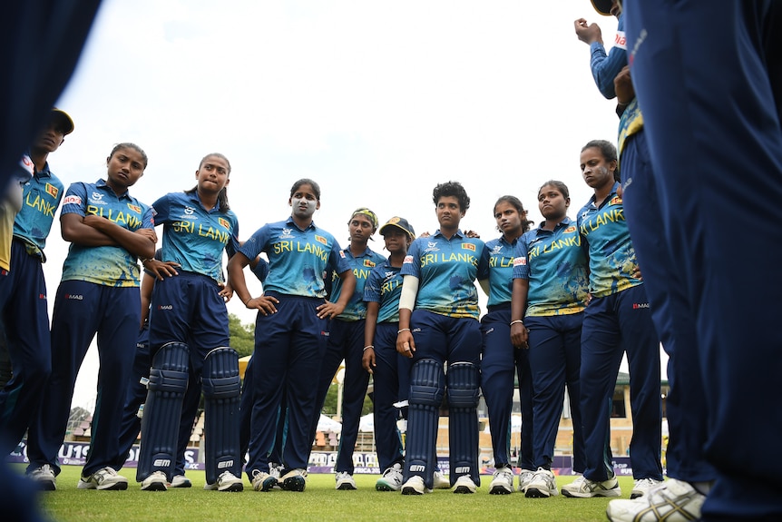sri lankan cricketers stand in a circle in a photo taken from a low angle inside the circle.