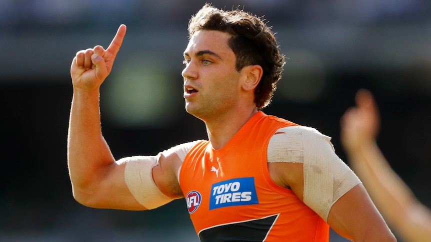 A GWS Giants AFL player points a finger in the air during a match in 2022.