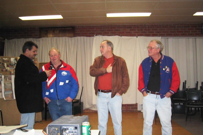 a man with a microphone addressing three older men