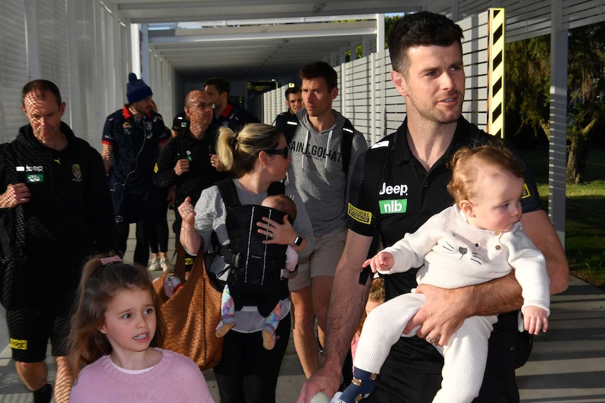 Richmond's Trent Cotchin carries a baby as another children walks with him at the AFL's hub on the Gold Coast in Queensland.