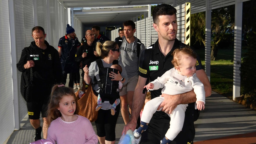 Richmond's Trent Cotchin carries a baby as another children walks with him at the AFL's hub on the Gold Coast in Queensland.