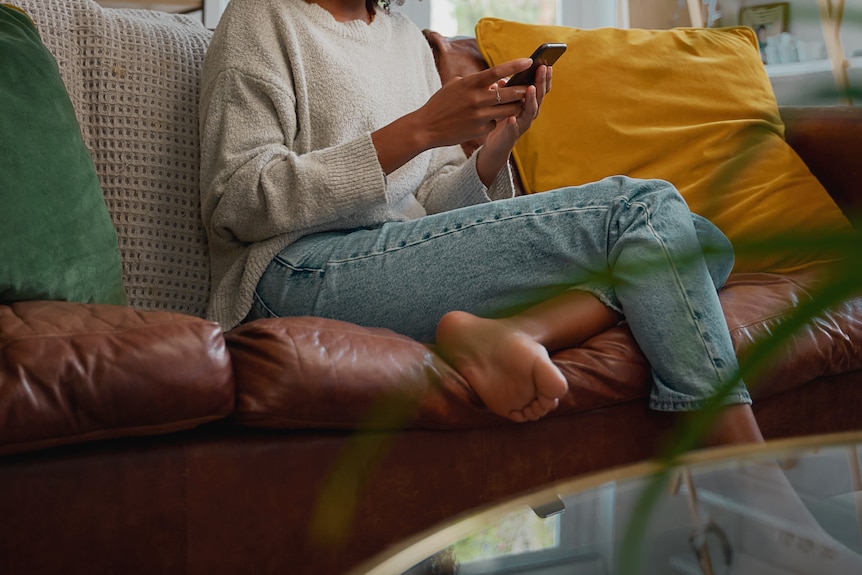 woman sitting on her couch looking at phone