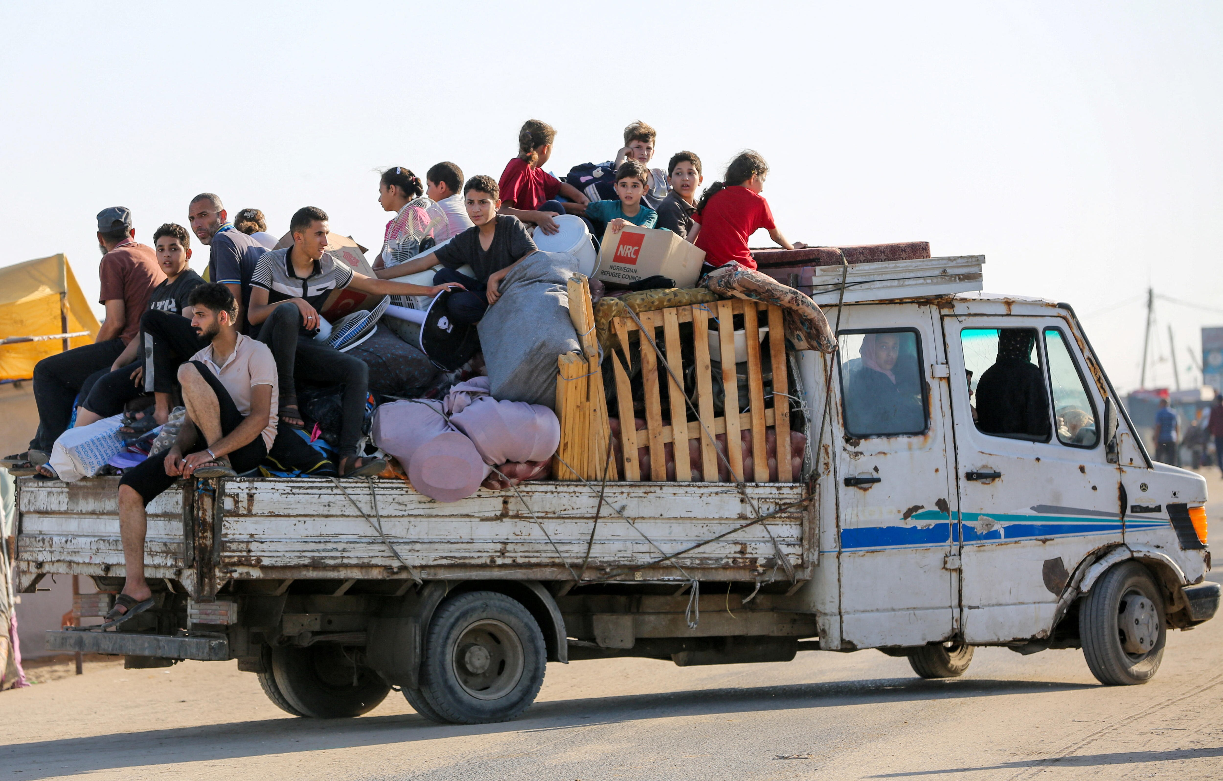A ute carrying a large group of people on the back and on the roof. 