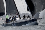 A black sailed yacht cuts through rough water with crew members moving onboard