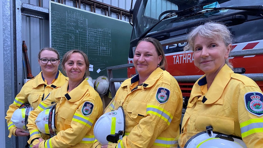 A group of women stand in front of a fire truck wearing RFS uniform and helmets