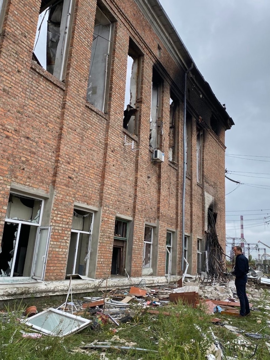 Investigator Nigel Pavoas looks at a charred building with debris strewn on the ground. 