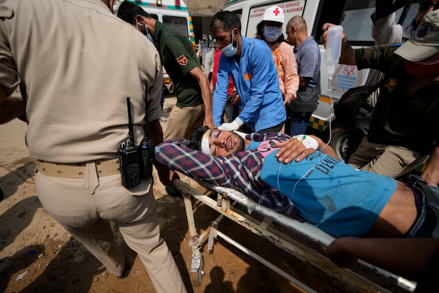 An injured man with a bandaged head is wheeled on a stretcher by several men.