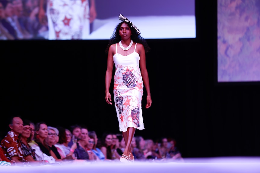 A young woman walks the catwalk runway modelling Indigenous designs.