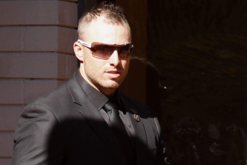 Ross Merrick, in a suit and wearing sunglasses, enters at Newcastle Court.