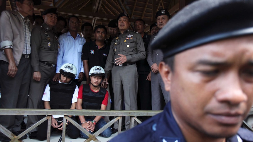 Thai police stand next to two detained Myanmar workers