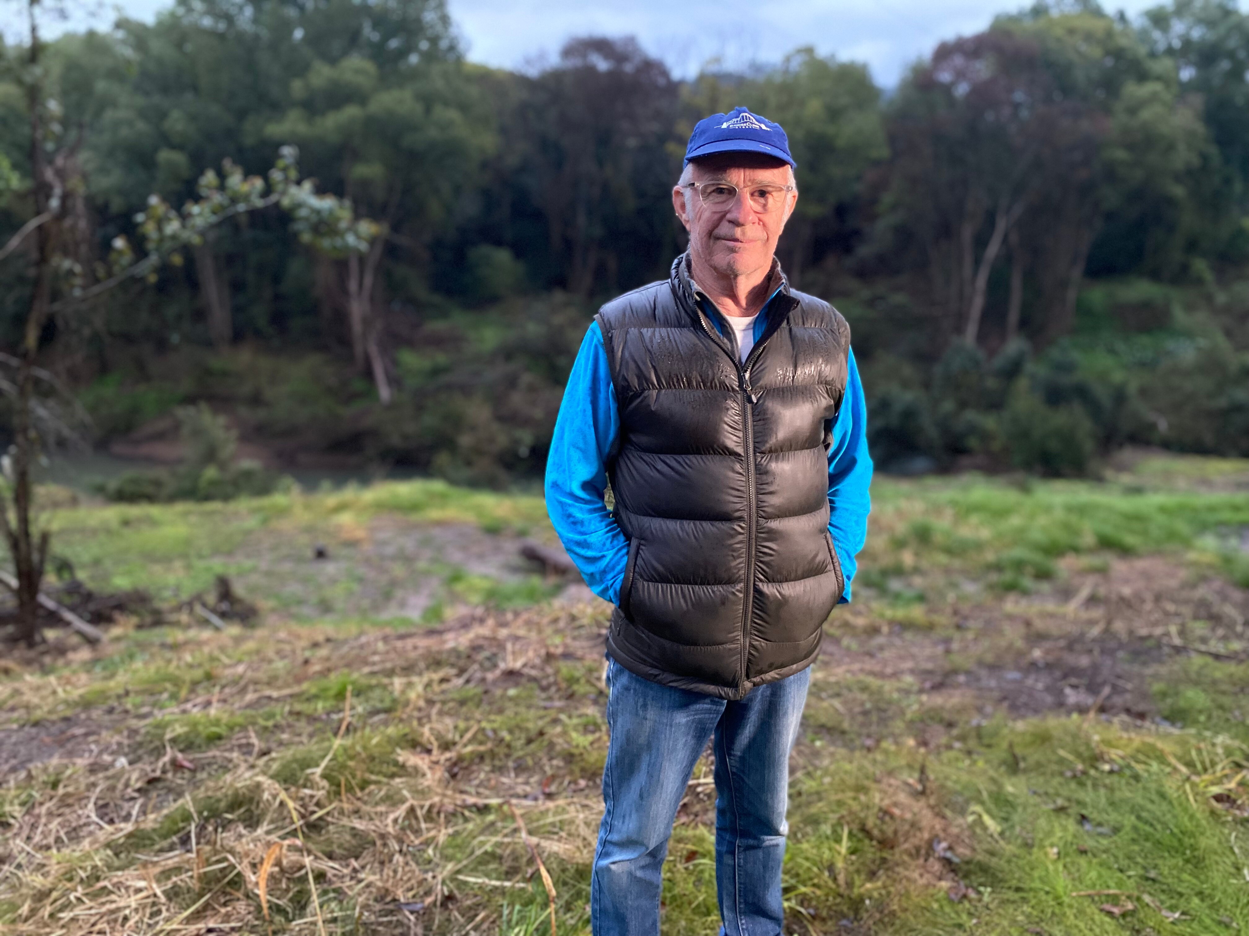 A man standing outside wearing a cap, a blue top and a black padded vest.