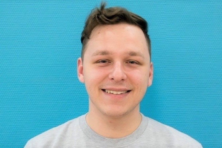 A close-up of a man with brown hair and brown eyes smiling.