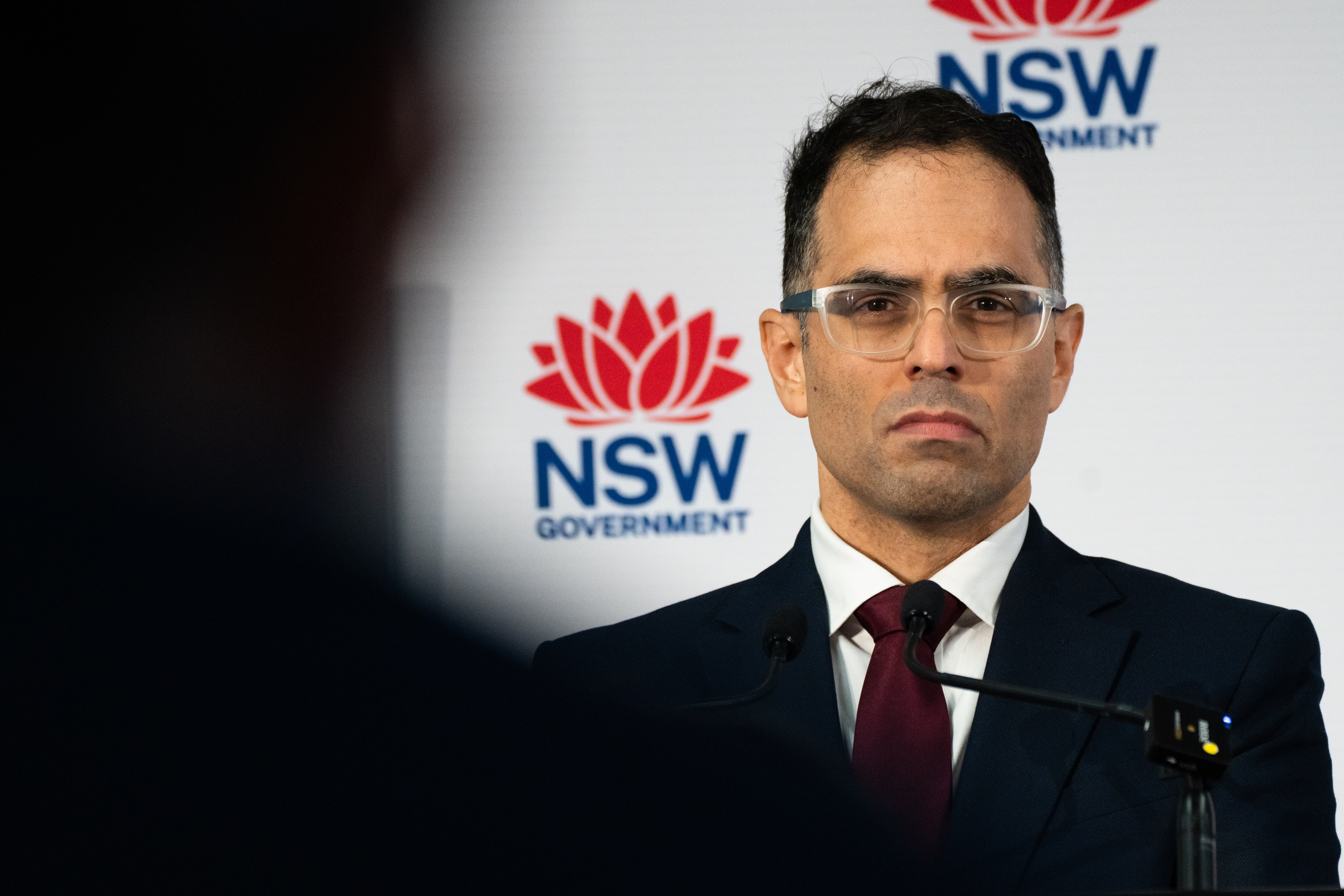Imagen de retrato de un hombre frente a un banner del gobierno de NSW