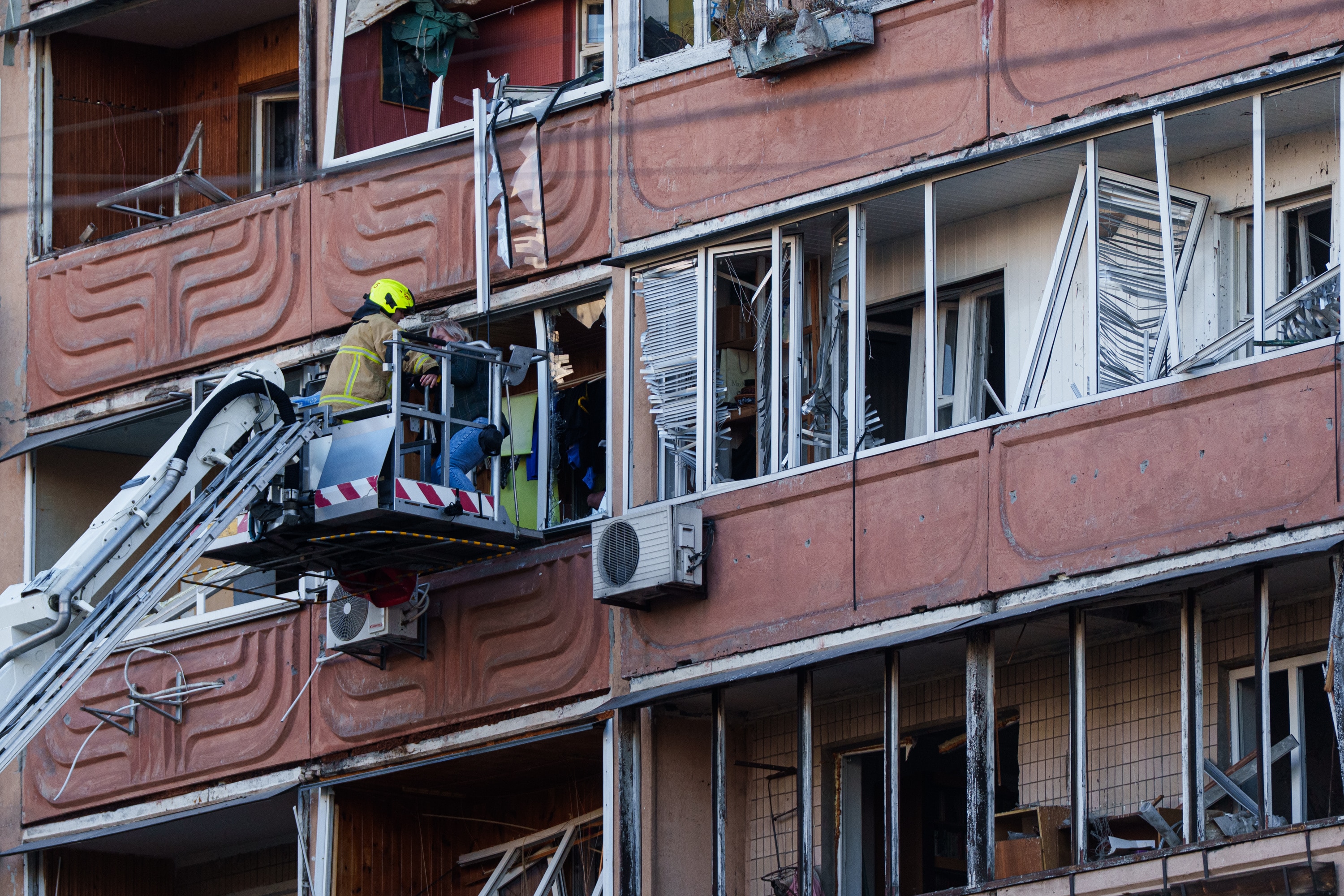 A fireman on a cherry picker trying to rescue a woman through the window of a damaged apartment complex.