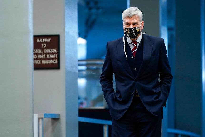 A man wearing a three-piece suit and face mask walks the halls of the Capitol.
