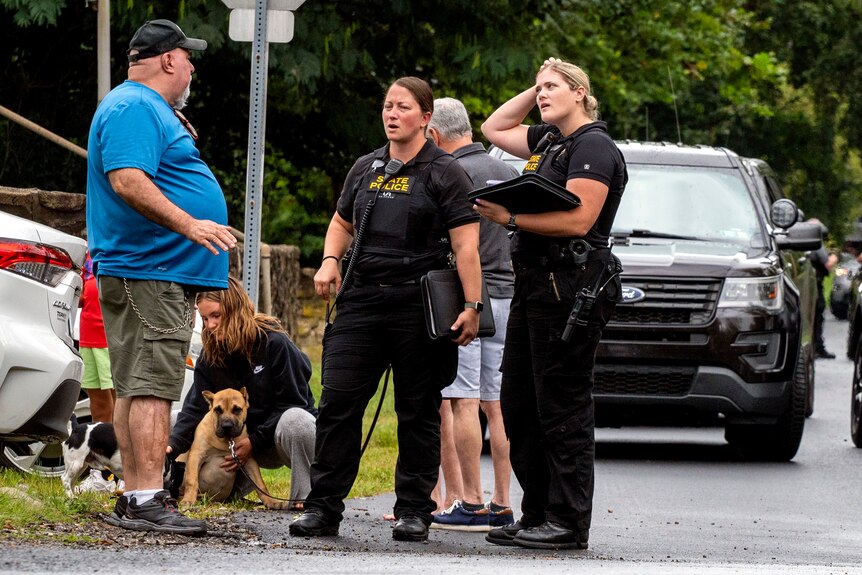 A man speaks to two women in Pennsylvania state police uniform