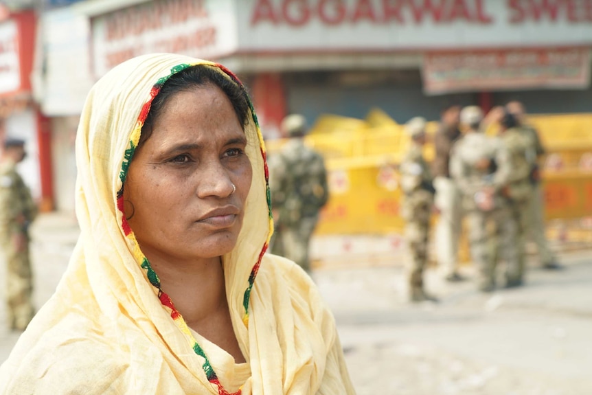 A women wearing a headscarf stares forward as police are seen behind.