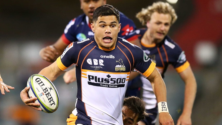 A Brumbies Super Rugby AU player holds the ball in his right hand as he makes a break against the Melbourne Rebels.