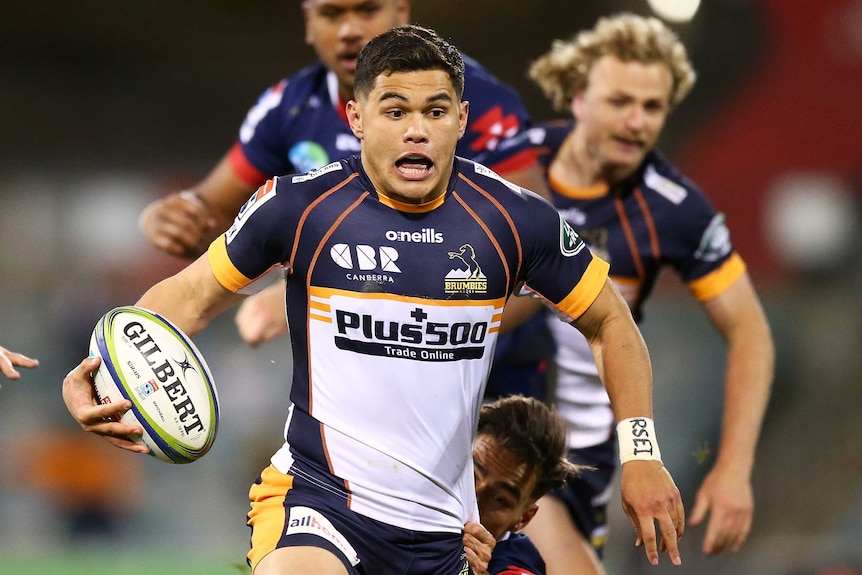 A Brumbies Super Rugby AU player holds the ball in his right hand as he makes a break against the Melbourne Rebels.