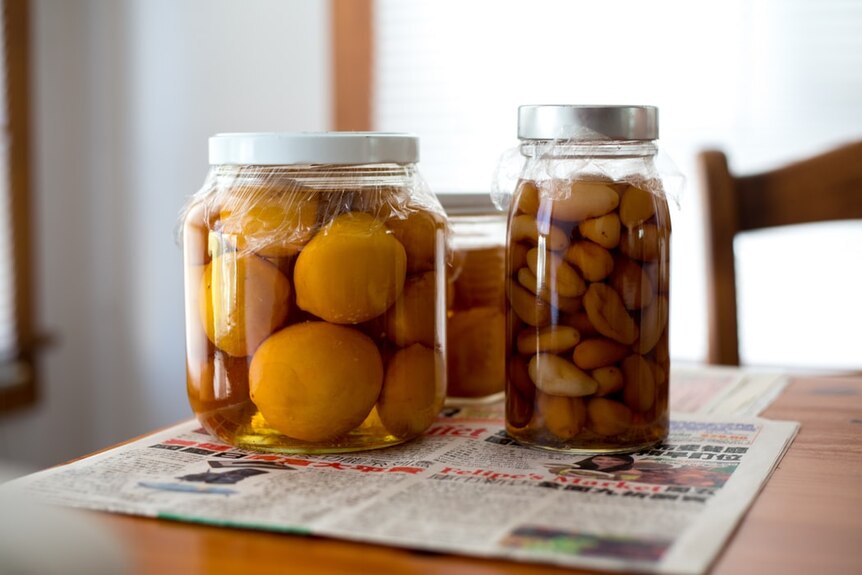 Three jars of pickles, including lemons and garlic, on a table on top of newspaper page for a story about pickling tips.