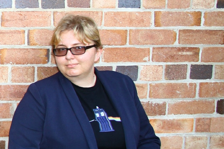 A woman wearing a blue jacket and a Dr Who tshirt standing against a brick wall