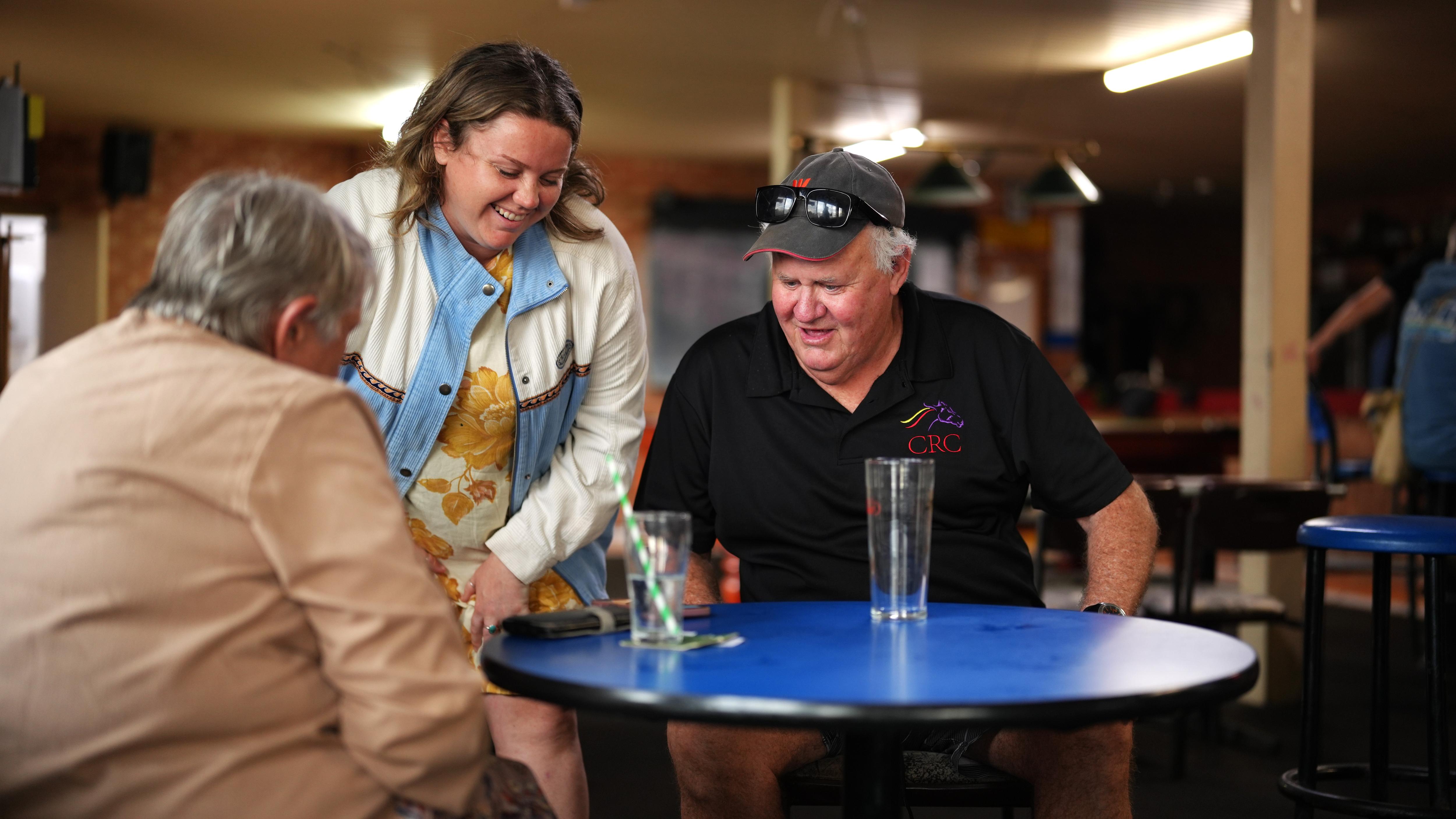 A young girl and a veteran man looking into a phone on a pub table.
