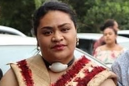 A young woman faces the camera in traditional cream and red Maori dress