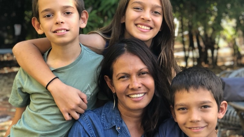 A mother with dark skin sitting and hugging three children with lighter skin.