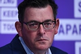 Premier Daniel Andrews, dressed in a suit at a press conference, looks with pressed lips towards a reporter.