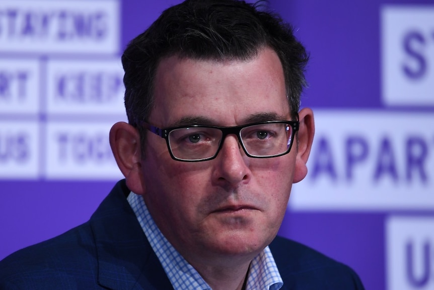 Premier Daniel Andrews, dressed in a suit at a press conference, looks with pressed lips towards a reporter.