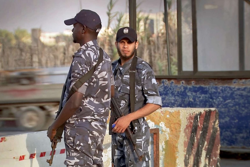 Two policemen holding guns stand at a checkpoint.
