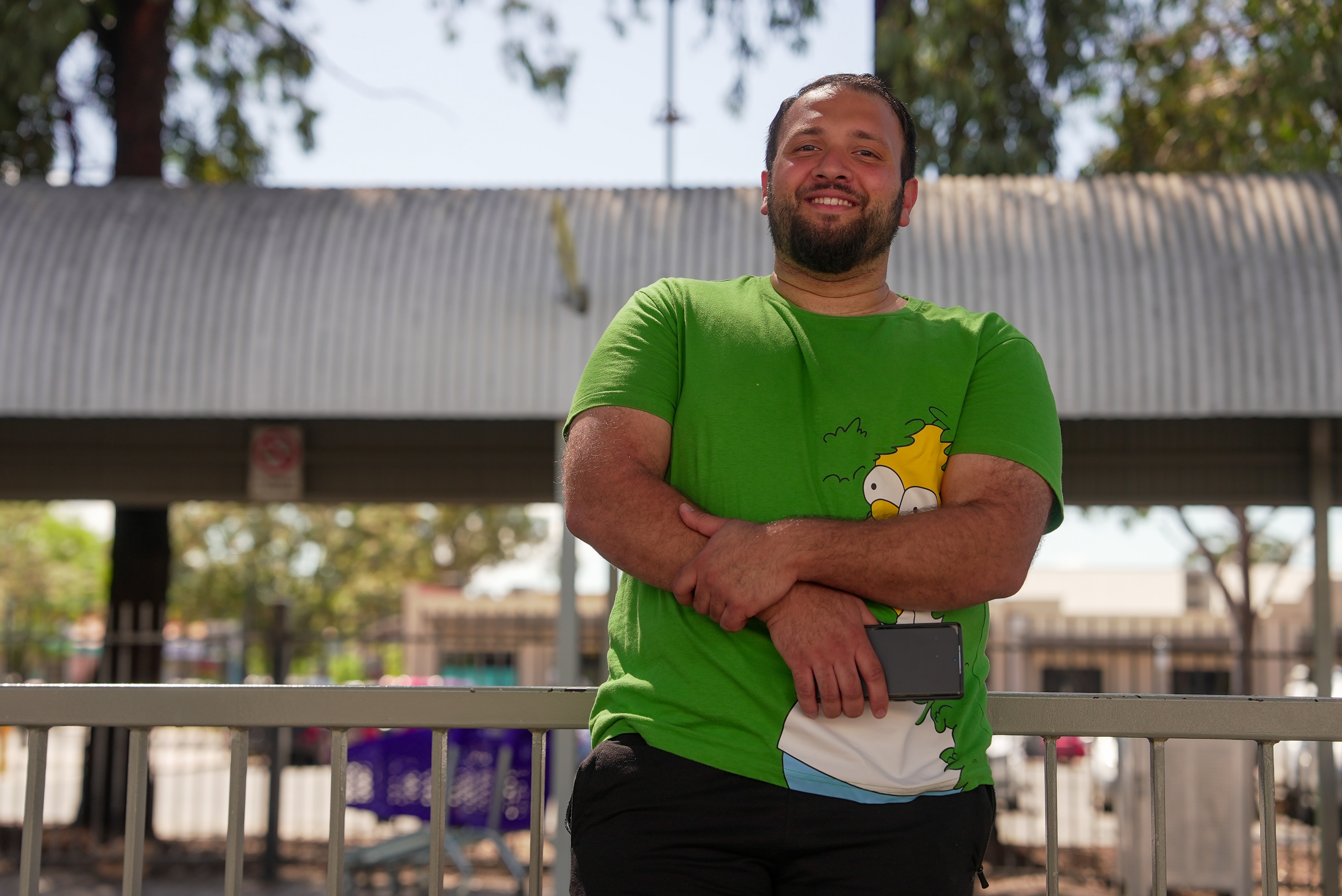 A man with crossed arms smiles in front of a bus stop