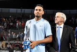 Nick Kyrgios holds the winners' trophy at the Brisbane International alongside Roy Emerson.
