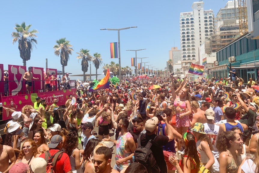 A crowd of people wearing bright colours celebrate on a street in front of a stage.