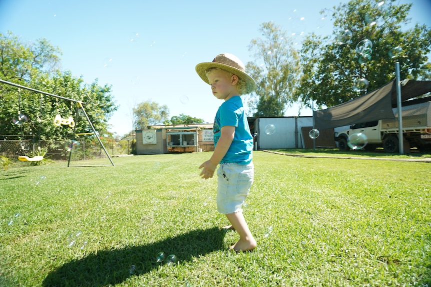 Toddler in blue shirt walking through bubbles in garden