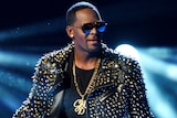 R Kelly wearing a studded leather jacket, holding a microphone.