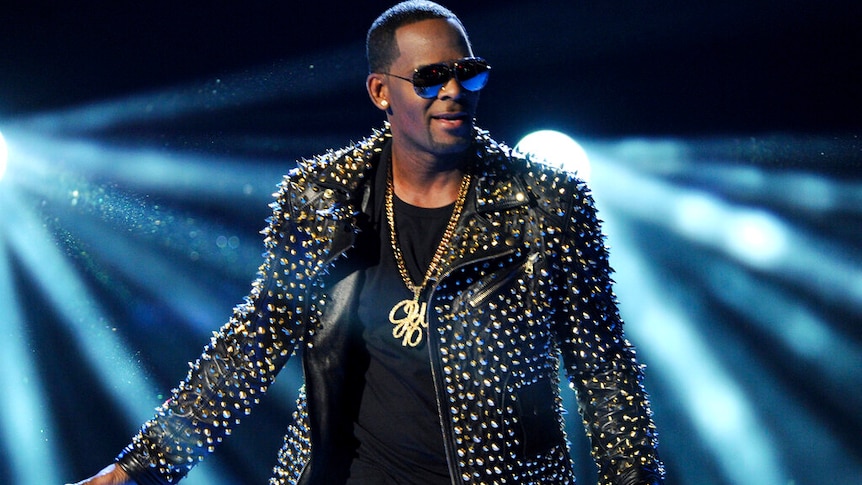 R Kelly wearing a studded leather jacket, holding a microphone.