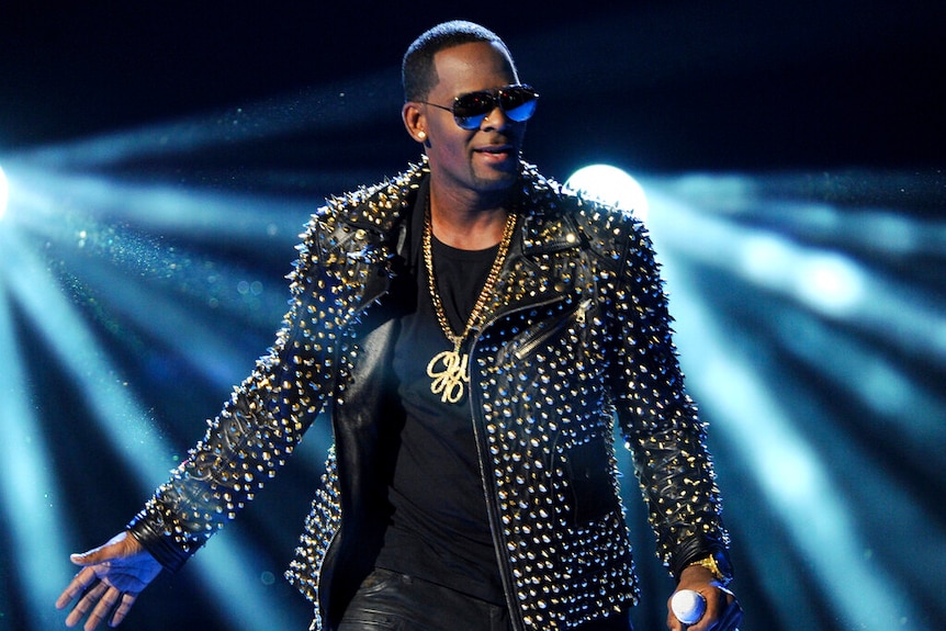 R Kelly wearing a studded leather jacket, holding a microphone.