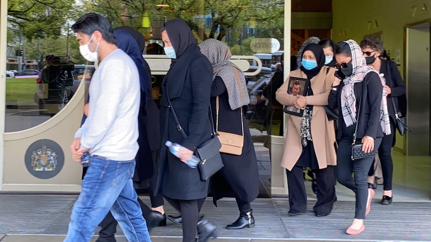 A group of people wearing masks walk out of a building with a gold sliding door