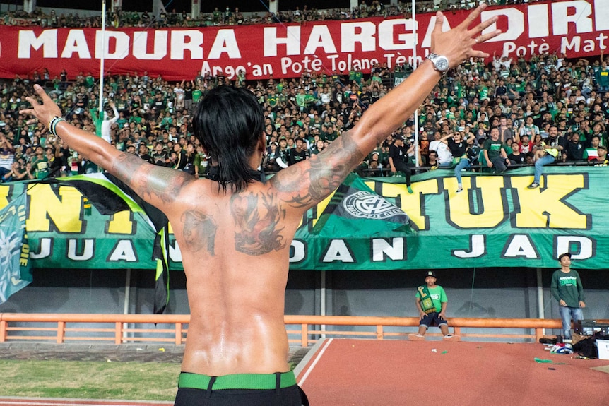 An tattooed entertainer raises his arms and faces the stadium crowd.