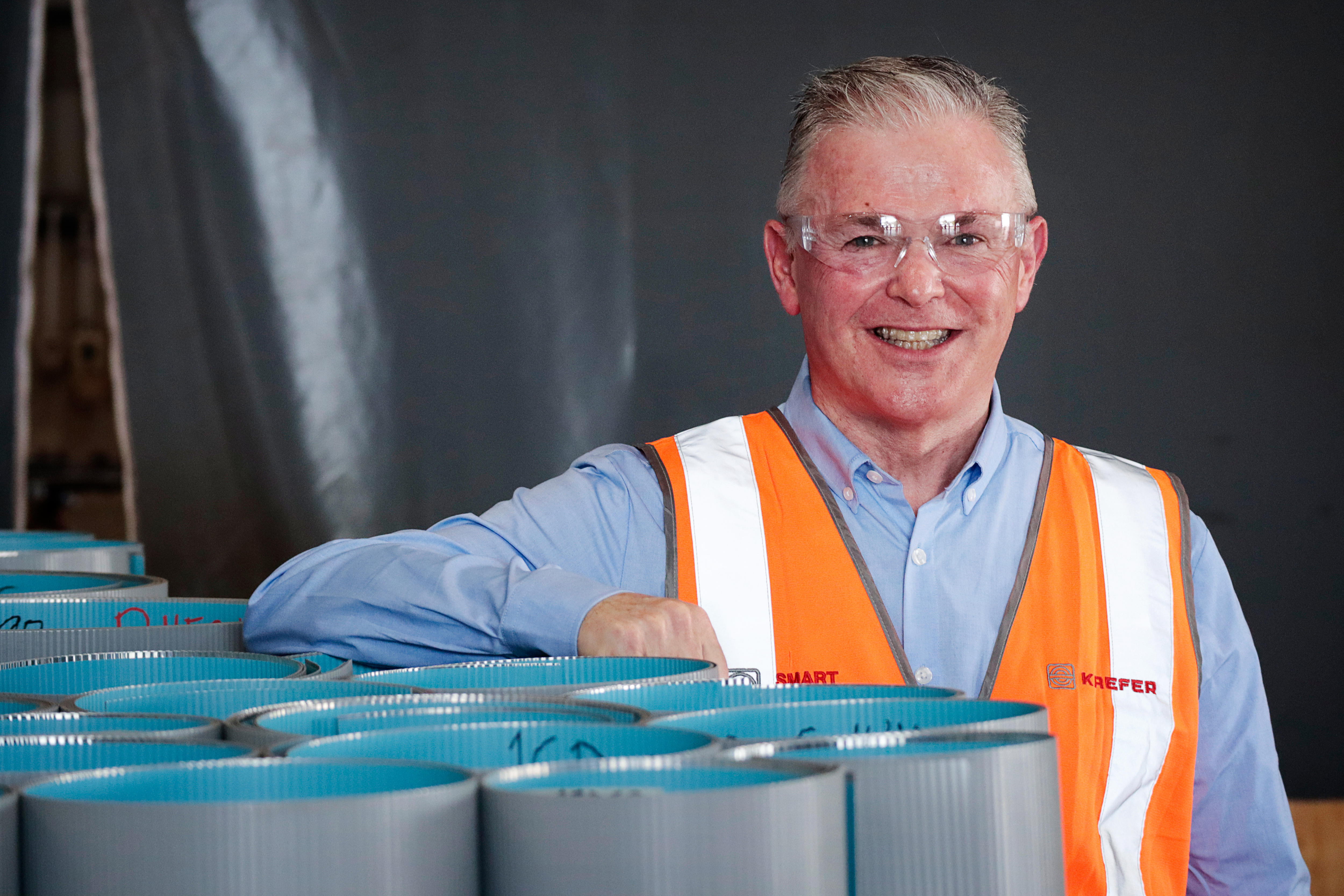 a man with grey hair wearing a hi-vis jacket over a blue collared shirt