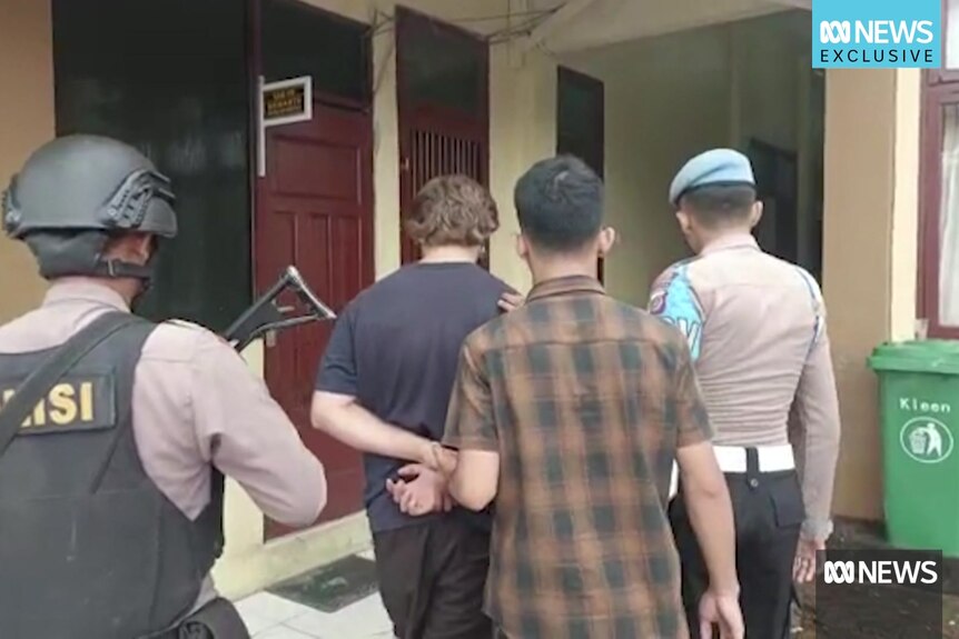 A young man in handcuffs is led away by police in Indonesia.