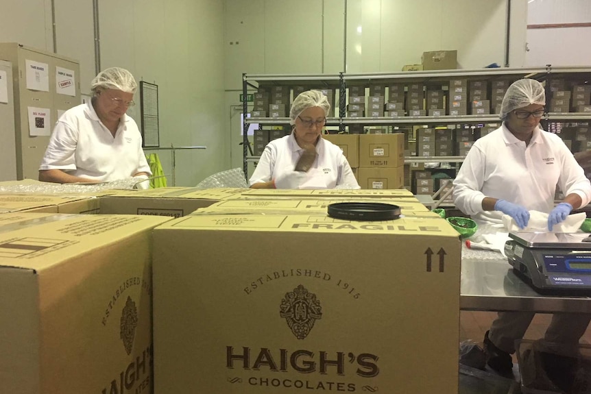 Workers wearing white coats and hairnets loading up boxes at the Haigh's Chocolates factory.