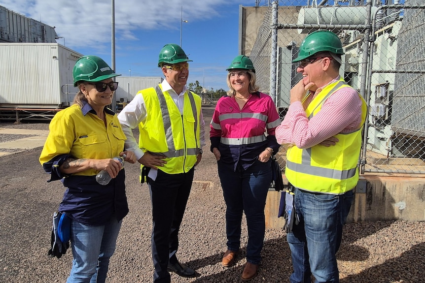Four people wearing hi-vis stand around talking at a power station. They are wearing hard hats.
